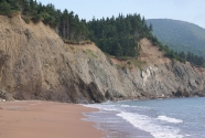 The north end of the beach originates at the base of sea cliffs, laid bare by erosion from waves and mass wasting.  The sands and gravels are carried south by the longshore current, building the baymouth bar, illustrating that a sedimentary beach is dependent on erosion for its sediments.