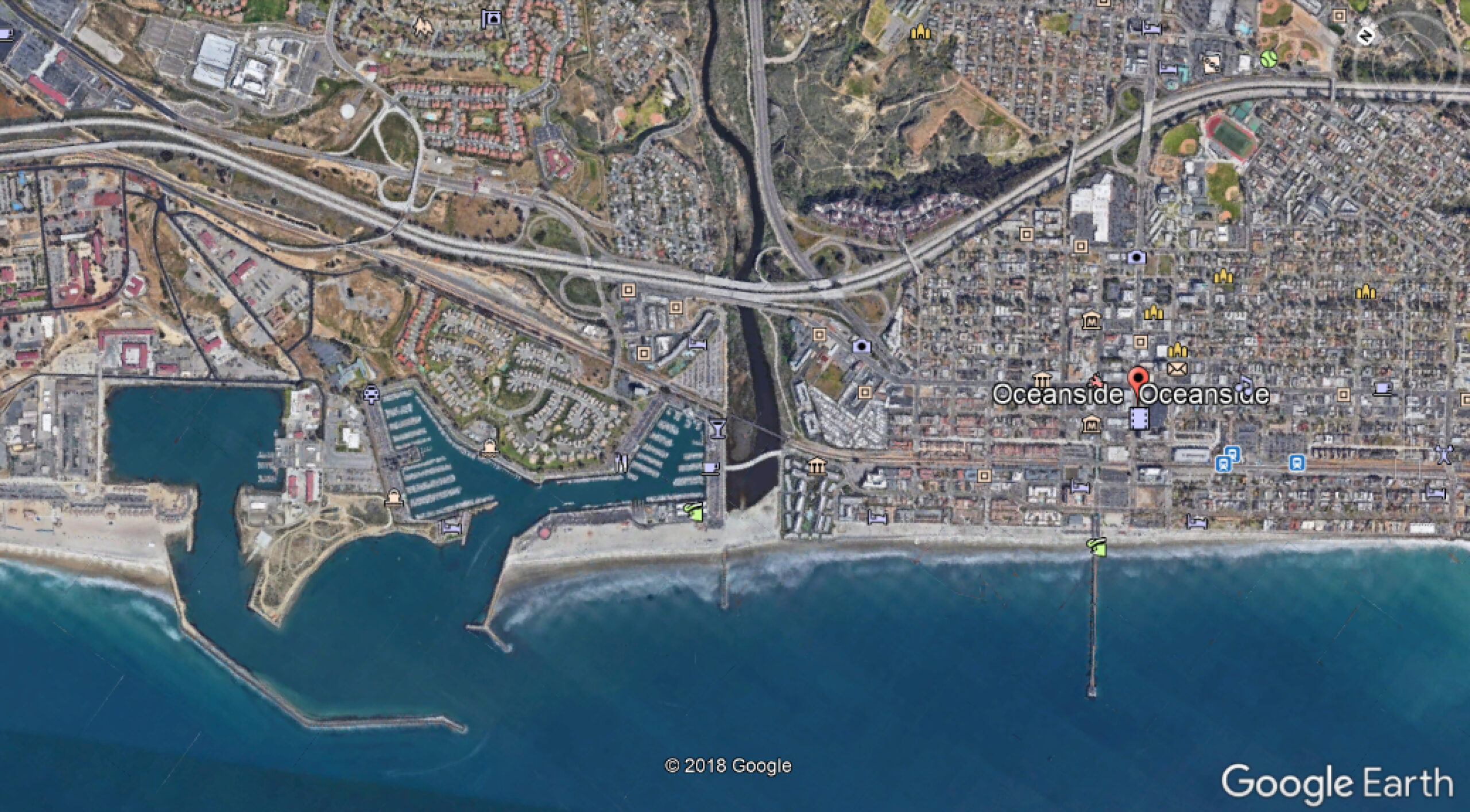 Screen shot from Google Earth showing the coast of Oceanside, California. From left to right you can see: 1) The 1942 Boat Basin; 2) The 1960s small boat harbor; 3) The 1961 groin at the mouth of the San Luis Rey River; and 4) the Oceanside pier. Note the buildup of sand on the upcoast sides of the boat basin (the beach on the far left side of the image) and the groin (the beach in the center), in addition to the much shorter beaches on the far right side of the image.