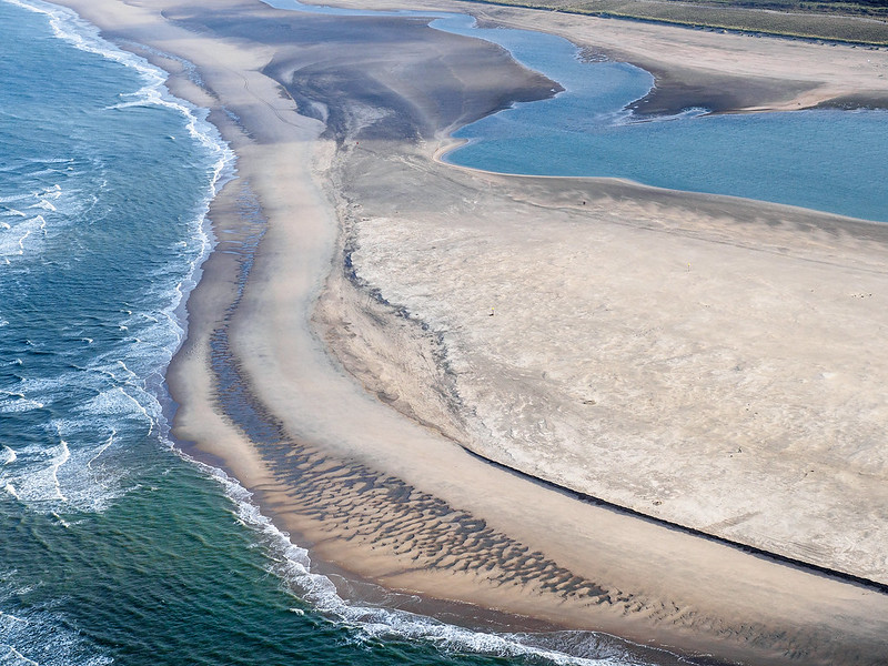 Aerial view of the middle of Zandmotor Beach, a large peninsula constructed on the coast of the Netherlands near the The Hague (by Joop van Houdt, courtesy of Rijkswaterstaat, Public Domain via Flickr).