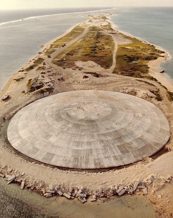 Aerial view of the Runit Dome (or Cactus Dome), Runit Island, Enewetak Atoll c. 1977-1980. The crater created by the Cactus shot of Operation Hardtack I was used as a burial pit to inter 84,000 cubic meters of radioactive soil scraped from the various contaminated Enewetak Atoll islands Courtesy of US Defense Special Weapons Agency, Public domain, via Wikimedia).
