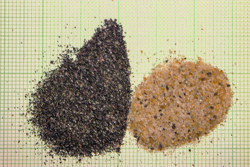 Figure 17. Photo of stamp sand (left) and natural quartz-rich beach sand (right) on mm-grid paper. Note that the black stamp sand is more poorly sorted in grain size (silt to granules), dominated by the dark colored crushed ore with only a trace of quartz and pink feldspar. In comparison, the natural beach sand sample, taken from just south of the jetties, is dominantly quartz (both clear and yellow-stained grains), moderately size sorted, with some black grains of stamp sand; evidence that the stamp sand is bypassing the jetties.