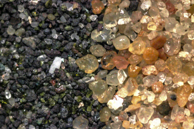Figure 18. Microscopic view comparing the poorly sorted, dark colored stamp sands on the left with the natural, moderately well sorted, quartz dominant sand on the right. The dominant stamp sand grains are sand-sized rock fragments, plus some green grains and a trace of quartz. The natural sand is almost entirely quartz, mostly subrounded to rounded, either clear or pinkish/tan from surface staining.