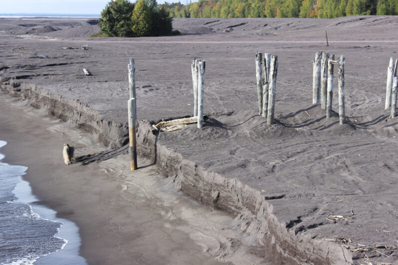 Figure 8. The wave-cut scarp near the exhumed posts of the old conveyor belt track has a vertical exposure of approximately 6 feet, providing a window to see cross-sections of the bedding and sedimentary structures in the water-laid waste deposits (See Figure 9).